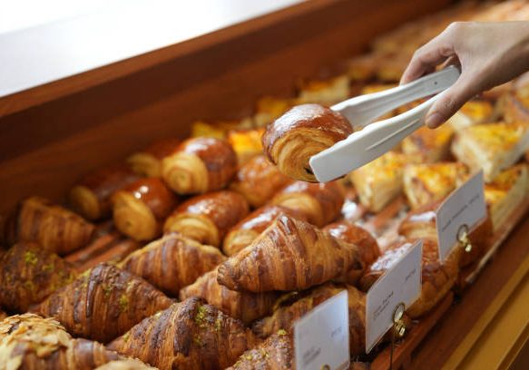Cropped image of an Asian young woman buying pastry from a cafe selecting holding a tray and service tong