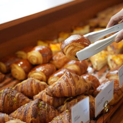 Cropped image of an Asian young woman buying pastry from a cafe selecting holding a tray and service tong