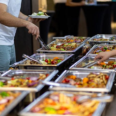 Guests fill their plates from a lavish buffet spread that includes an assortment of colorful dishes, salads, and entrees during a communal dining event.